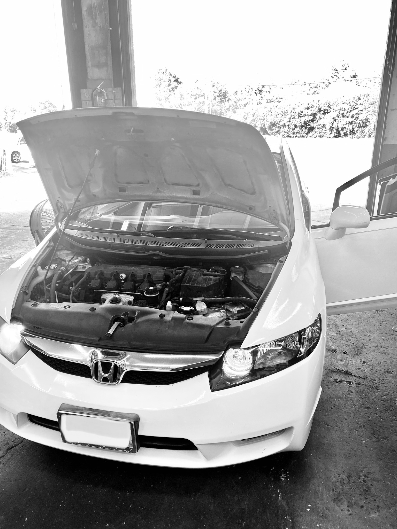 A white Honda sedan with its hood open, revealing the engine compartment, inside a garage.