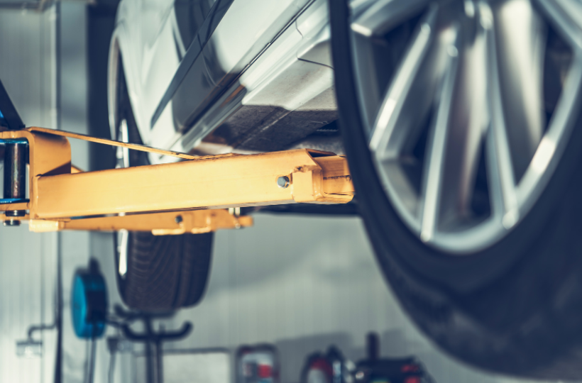 A close-up view of a car being lifted by an orange hydraulic lift in a garage, showcasing the underside and a wheel.